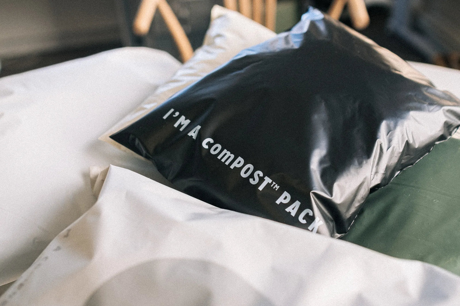 A black compostable mailer with white text "I'M A comPOST™ PACK" sits on top of two other packages.