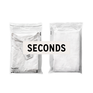 Front and back of a transparent Better Packaging POLLAST!C poly garment bag, containing a white tee shirt on a transparent background with a graphic label "Seconds"